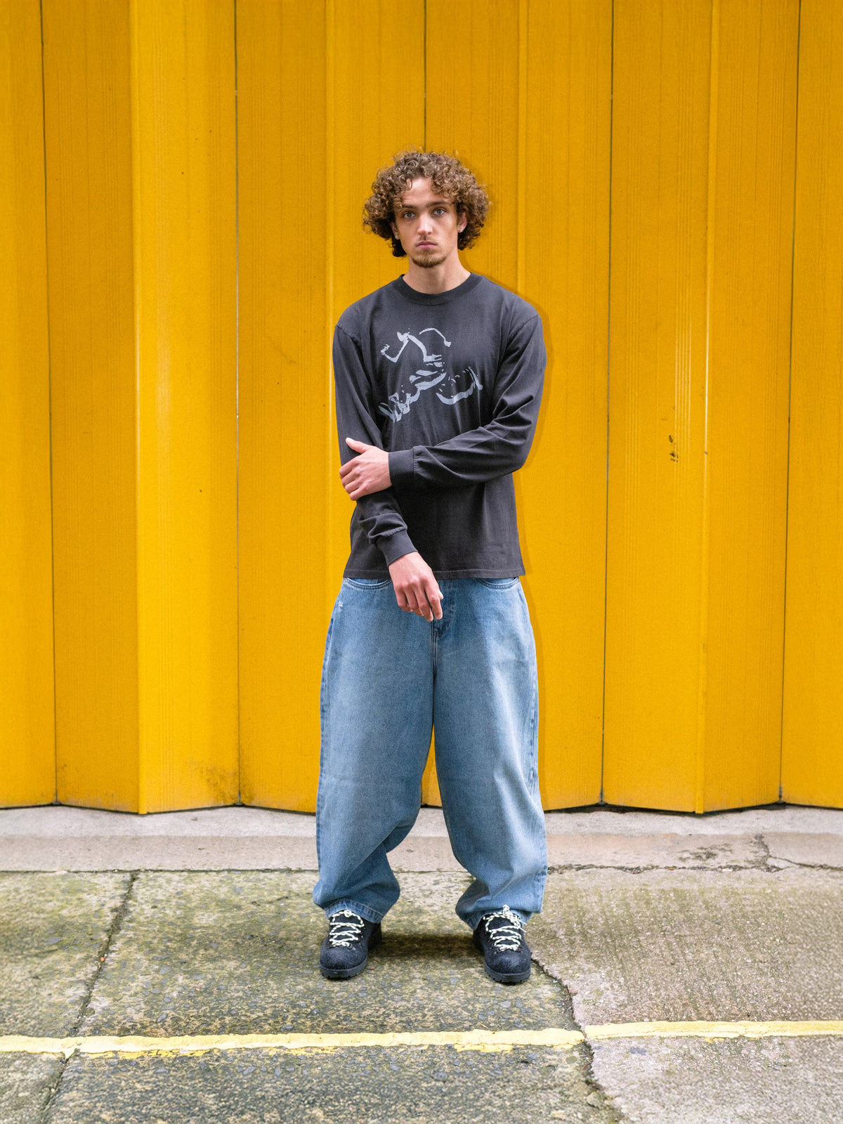 Model wearing denim pant fray and runnin' man t-shirt infront of yellow shutter door