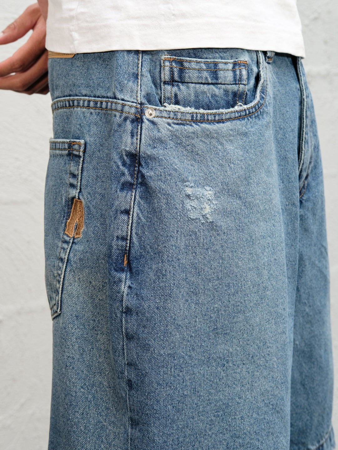 Model wearin Denim Short | Fray paired with 95's and a white t-shirt close up of hand-fraying