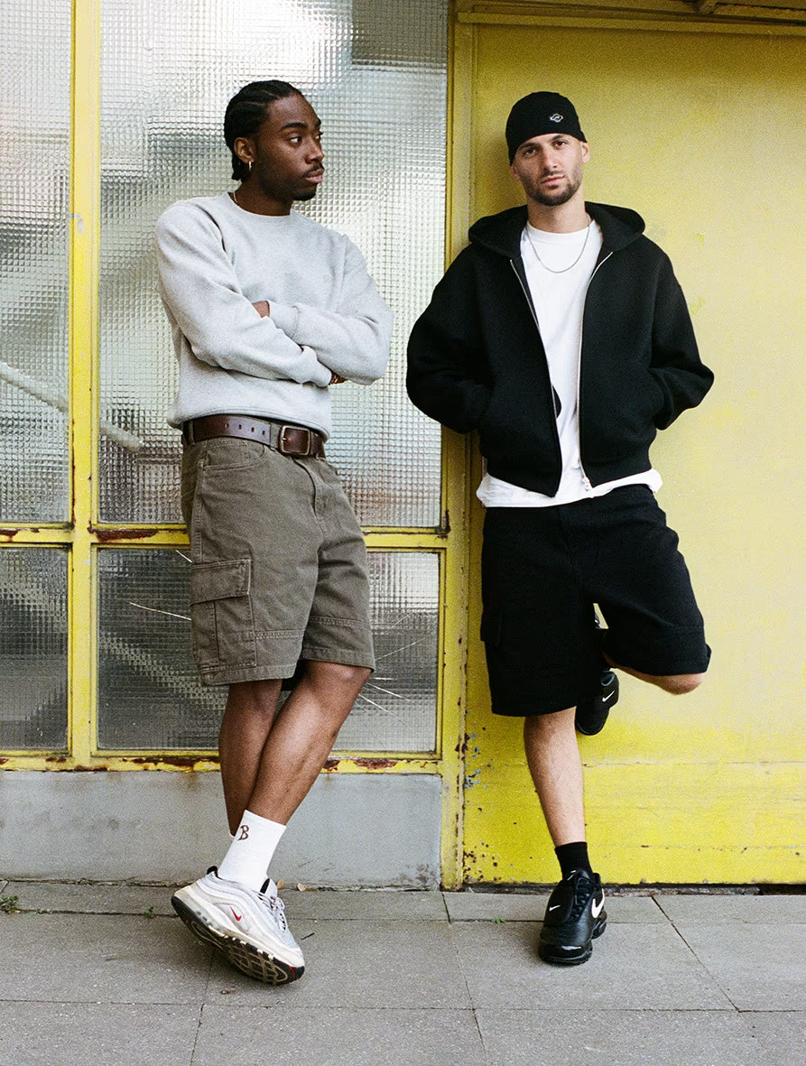 Two men standing against a yellow wall with a glass panel