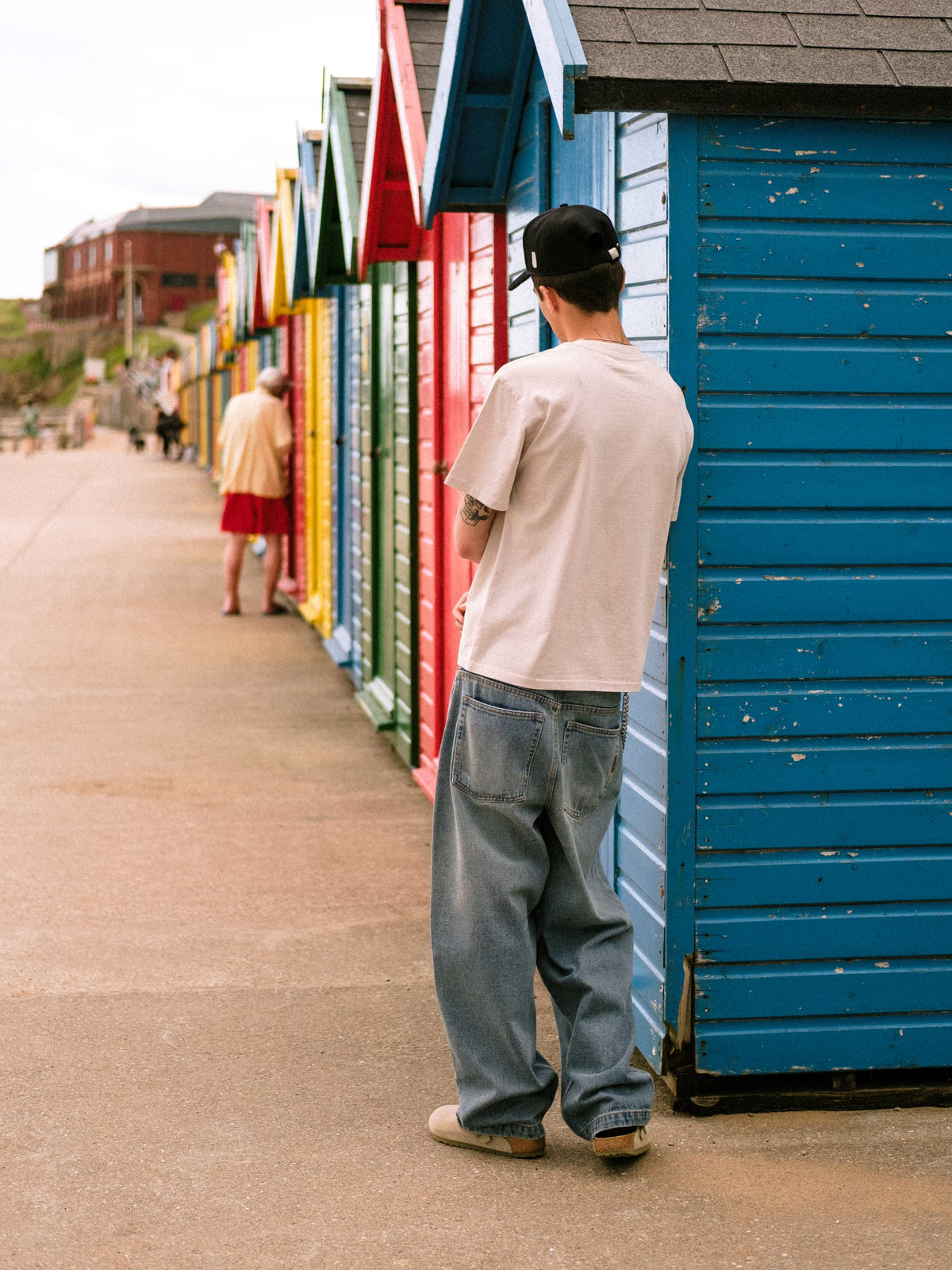 Model leaning on beach huts at peer wearing denim pant fray and bone t-shirt
