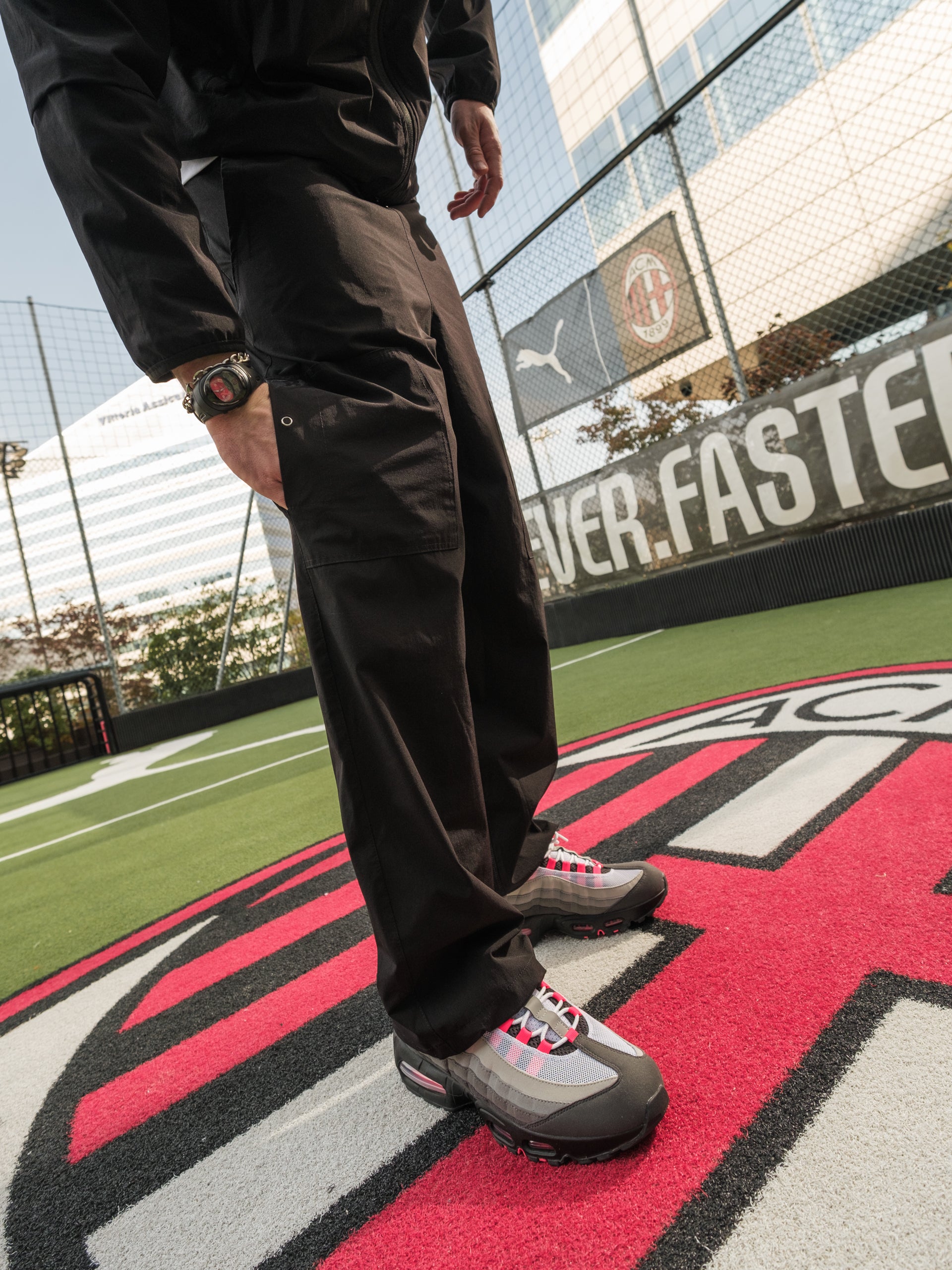 Person wearing dark pants and shoes on a sports field with visible branding.