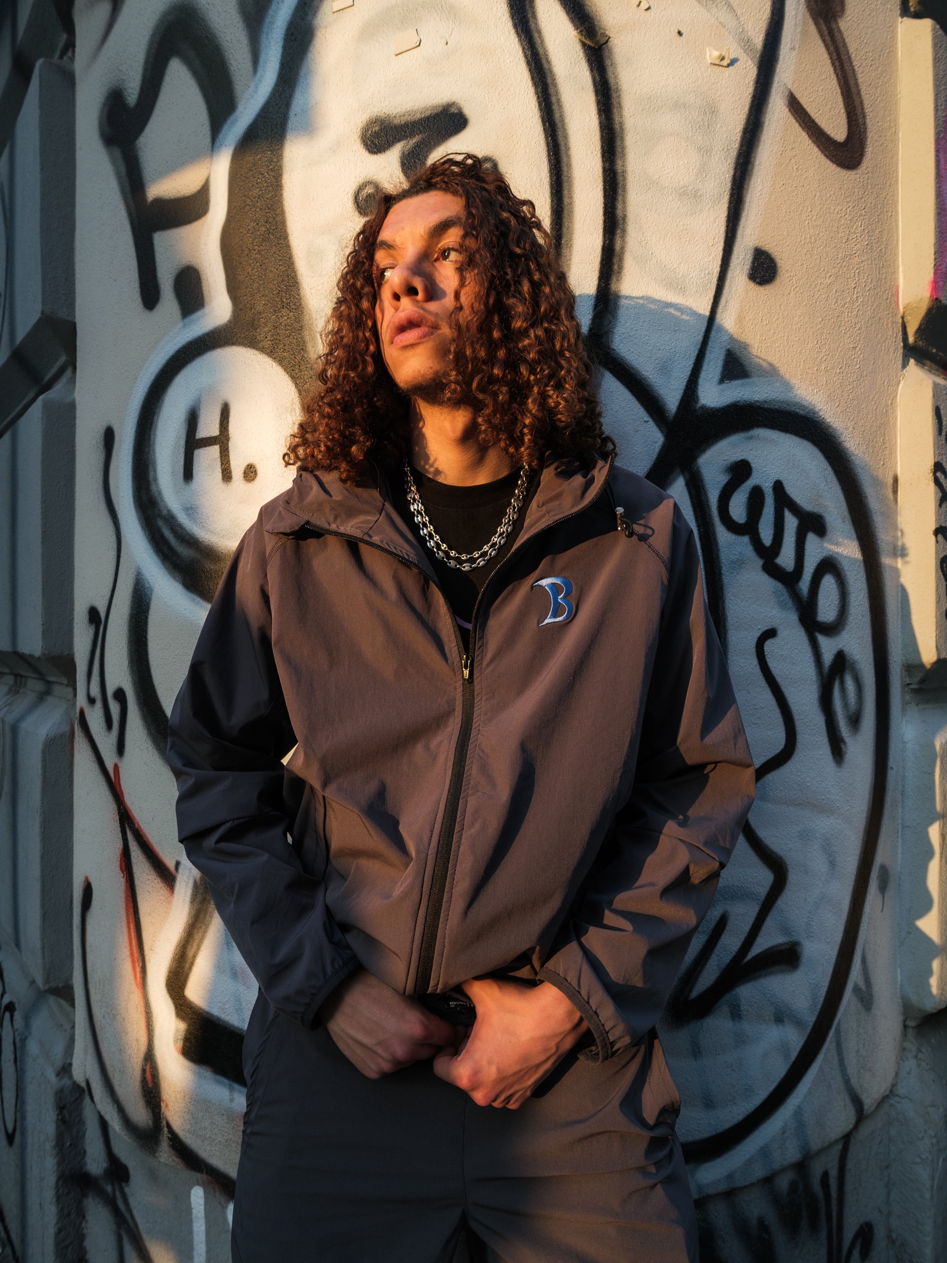 Person wearing Baggys Oxide Grey jacket with a brand logo in front of a graffiti-covered wall