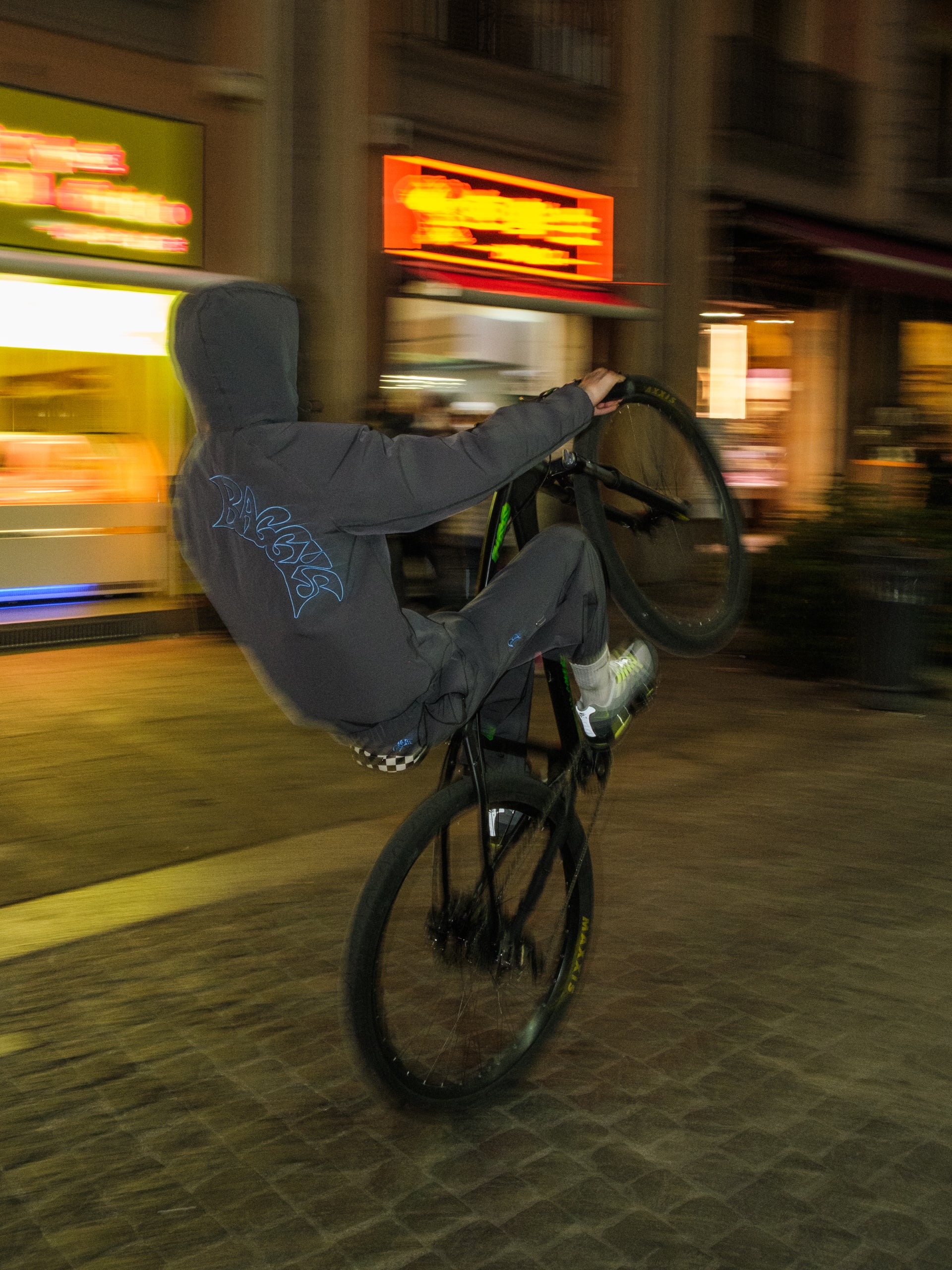 Person performing a bike trick on a city street at night with blurred lights in the background