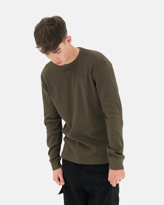 Person wearing an olive green long sleeve t-shirt on a white background