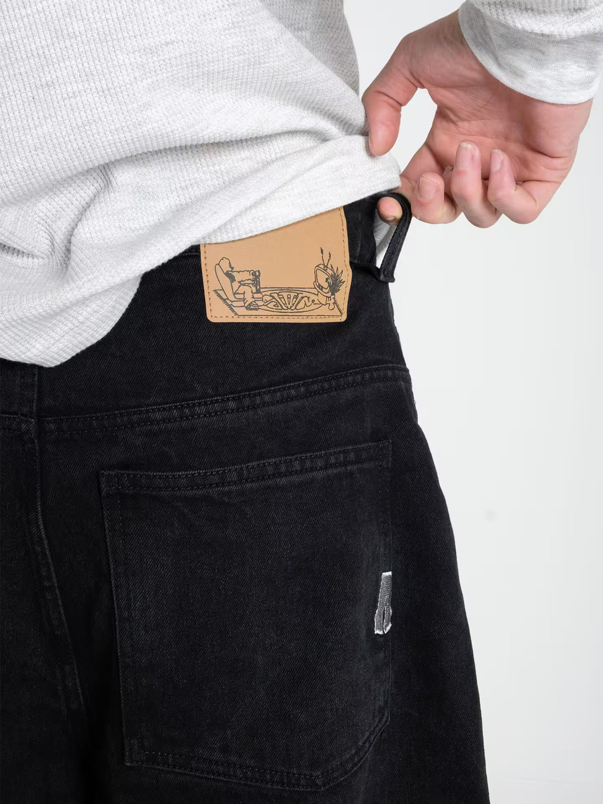 Person wearing Baggy Jeans Pitch denim, showing a close up of the belt patch and wash