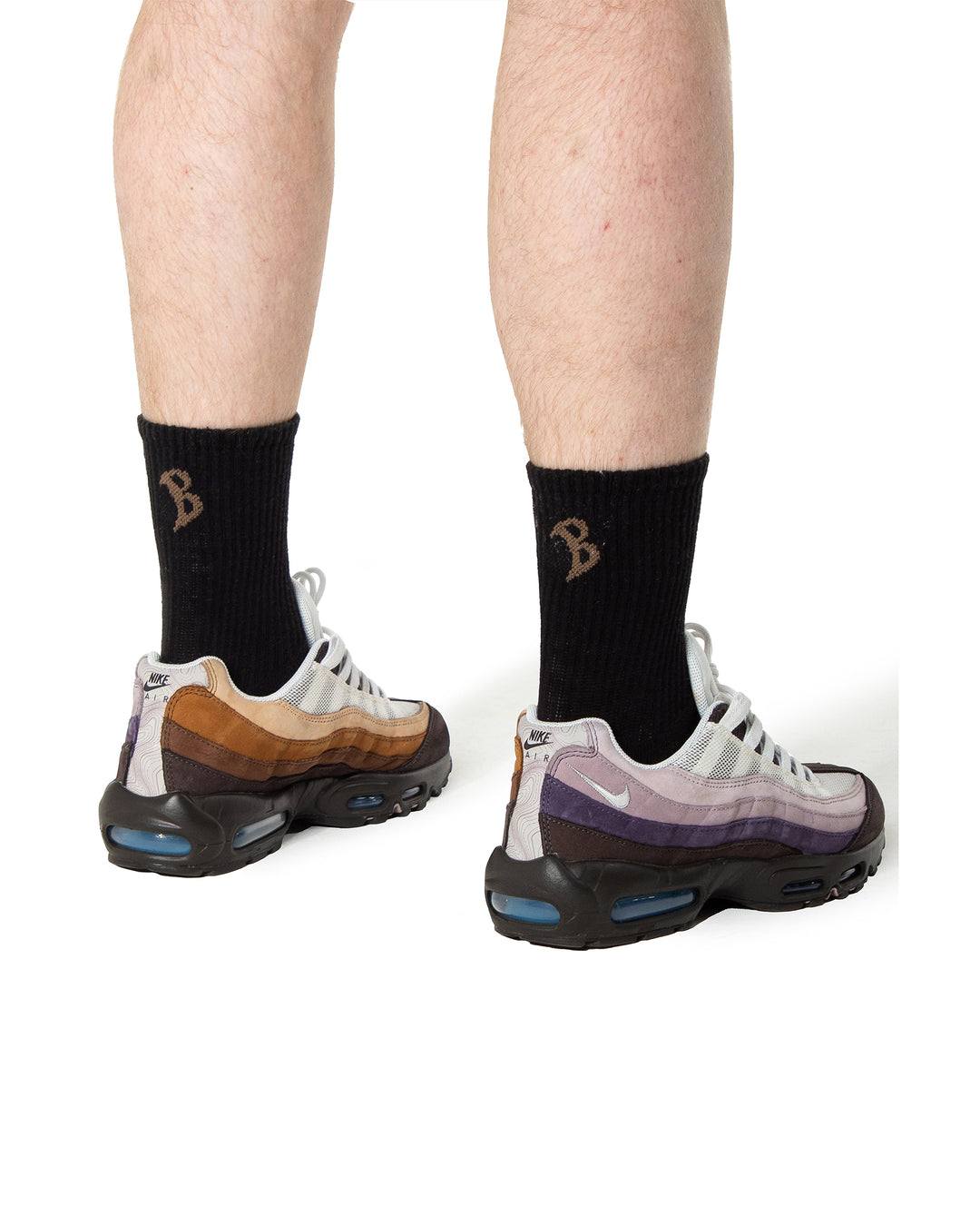 Person wearing black socks with a logo and colorful sneakers on a white background