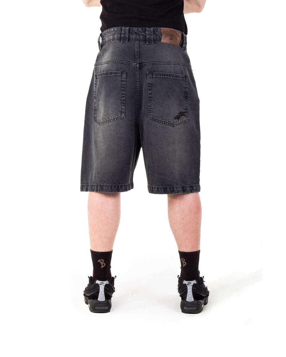 Person wearing black denim shorts on a white background
