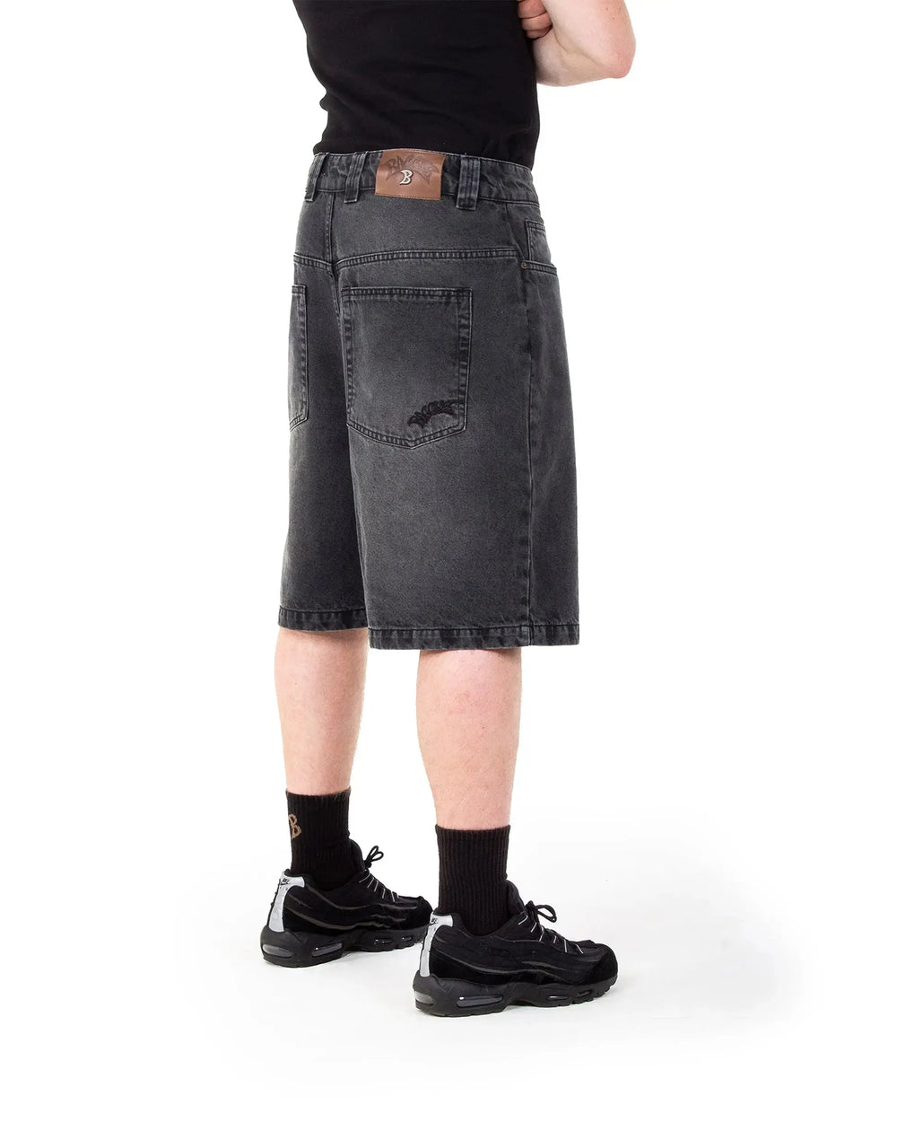 Person wearing black denim shorts on a white background