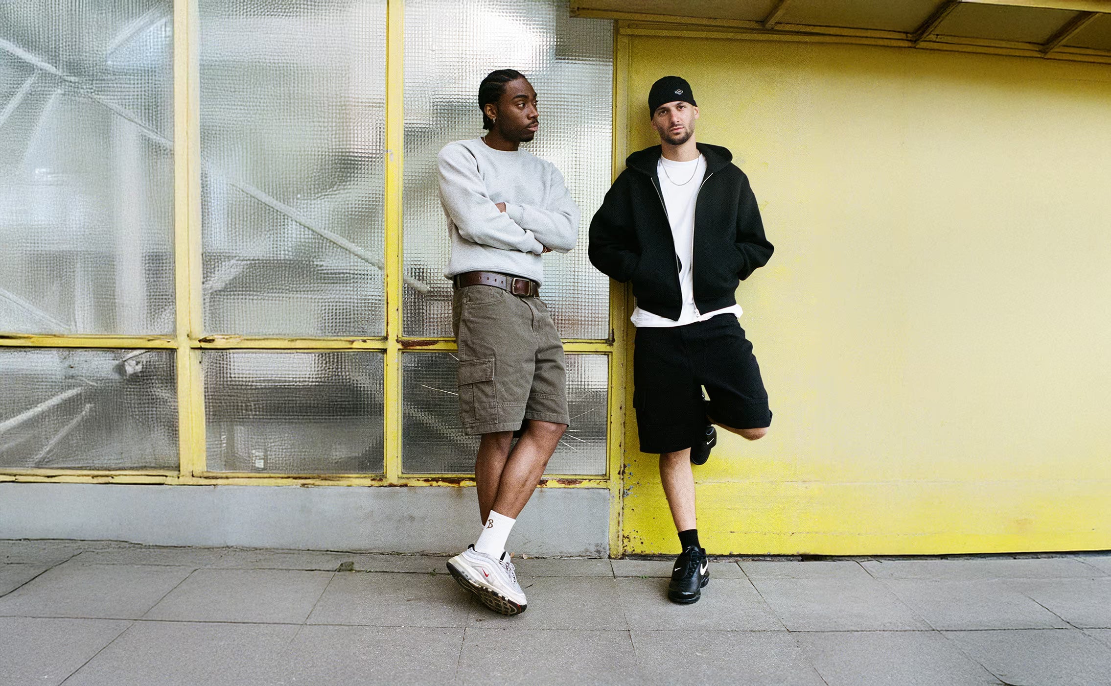 two men standing wearing cargo shorts, infront of a glass panel