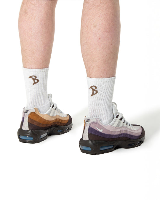 Grey socks with brown logo worn with black and white sneakers on a white background